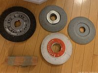 Five grinding and wire brush wheels and an abrasive bar arranged on wooden floor showing their size and condition.
