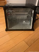 Front view of compact black rotisserie oven with glass door showing spinning spit inside.