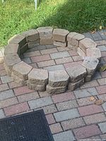 24 tan/brown textured rectangular landscaping stones arranged on brick pavers in a circular shape.