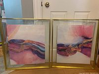 Pair of framed abstract paintings side by side, each featuring vibrant wave designs in pink and purple hues within gold metallic frames and glass surfaces.