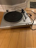 Front angle showing the turntable platter, tonearm, and front controls with power cord attached.