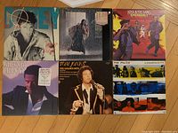 Photo showing all 6 vinyl record album covers arranged in two rows on a wooden floor, including Corey Hart, Gloria Estefan, Kool & The Gang, Gregory Abbott, Tom Jones, and The Police.