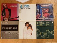 All six vinyl record album covers laid out on wood floor showing artists and titles