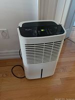 Front view of the white Whirlpool Gold Series dehumidifier showing the front grille and power cord on hardwood floor.