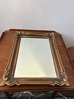 Rectangular antique bronzed metal framed mirror lying flat on a wooden table showing full frame detail and bevelled glass.