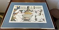 Framed lithograph art print by Maurice Sendak showing three bakers with speech bubbles, framed in wood and blue mat, placed flat on couch.