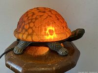 Front view of figural turtle lamp illuminated showing orange mottled stained glass shell and metal turtle base