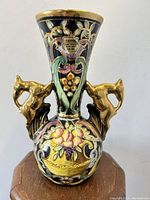 Front view showing pitcher with black base, floral and fruit basket painted decoration, and two gold antelope handles.