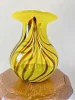 Front side view of yellow and brown swirl art glass vase sitting on wooden surface.