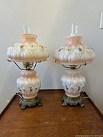 Pair of vintage electrified trilight hurricane lamps shown off with pink blush blown-out quilted glass, floral details, clear chimneys, and ornate metal bases, viewed under natural light