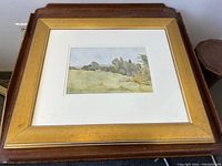 Full view of framed painting showing gold frame, white mat, and landscape painting with sky, trees, and grass hill.