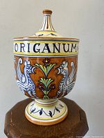 Front view showing hand-painted mythical creatures and floral design on reddish-brown background with ORIGANUM label.