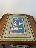 Framed Chinese silk embroidered wall hanging showing full piece on wooden surface with visible embroidery and frame details.