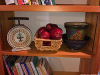 Shelf view showing antique Hanson utility scale, basket with red plastic apples, and two pottery planters