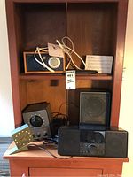 Shelf with Troll Audio Model One table radio, Logitech radio, Advent FM receiver and Advent speaker. Slate stone battery-operated clock and remotes on shelf.