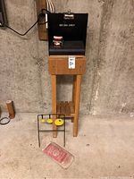 Full view showing the black metal box catcher on the wooden stand, metal spinning target on the floor, and bag of lead shot