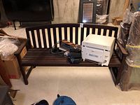 Photo showing front view of dark wood bench with some items placed on seat. Clear view of curved backrest and armrests.