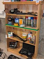 Front view of unfinished wood bookcase with multiple shelves containing various tools and spray cans, illustrating bookcase condition and dimensions.