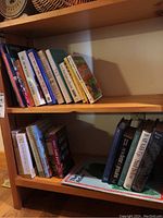 Books on two wooden shelves showing various titles including cookbooks, fiction, and historical references, with a Maine atlas mat on bottom shelf.