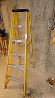 Yellow Keller folding ladder with five aluminum steps and fiberglass frame against concrete wall.