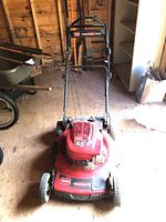 Front view of red Toro lawn mower with upright handle in wooden shed.