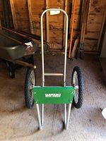 Front view of the log hauler showing the handle and the green branded plate with two large wheels.