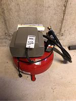 Front view of Porter-Cable pancake air compressor with power cord and air hose coiled beside it, placed on concrete floor against wall.