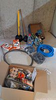 Full lot view showing yellow-handled plunger, wooden-handled plunger, packaged clamps and connectors, blue hose, downspout strainer, and box of assorted hardware.