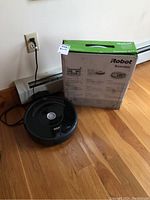 Photo of the black iRobot Roomba 675 robotic vacuum next to its original box with green and white design.