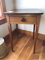 Front view of the wooden side table showing drawer with round knob and scuffed top surface.