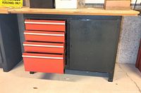 Front and left side view of the tool cabinet showing four red drawers, black cabinet door, and plywood top on a concrete floor.