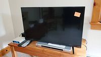 Front view of Vizio 32-inch TV on wooden table with remote and other electronics.
