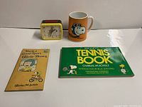 Overall view of the lot including musical mug, clock, and two books on a white surface.