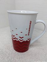 Front view of the Starbucks mug showing the red Starbucks logo printed vertically and red geometric pattern on the white ceramic body.