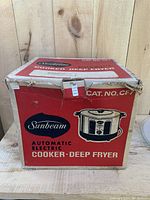 Front and side view of the original red and white box featuring the Sunbeam brand, product description, and image of the cooker deep fryer.