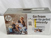 Front of sealed box showing HP branding, image of a couple and the printer, with text 'Smallest All-in-One Printer'.