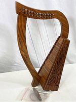 Full view of the Irish Celtic harp showing the carved wooden body, strings, tuning key and extra strings in a plastic bag.
