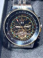 Close-up front view of Jaragar watch showing black and gold large dial with subdials and mechanical movement window at 6 o'clock, inside protective foam box.