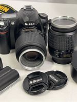 Nikon D50 camera body with 18-55mm zoom lens attached and 55-200mm zoom lens beside it, including lens caps and battery.