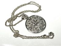 Full view of silver chain and pendant laid out, showing chain design and pendant's intricate floral-geometric pattern with small stones.