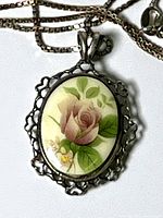 Close-up of oval sterling silver pendant with painted pink rose design, showing details of the floral painting and silver openwork setting.