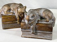 Pair of vintage cat on books cast metal bookends with brown antique patina on white background.