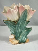 Overall view of the pink double tulip shaped pottery vase with green leaves and beige base.