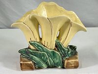 Front angle view of vintage McCoy pottery vase shaped as three yellow calla lilies with green leaves base and brown accents.