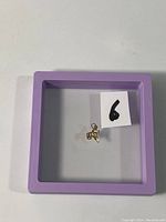 Tiny gold pendant placed inside a purple display frame with a number '6' label visible.