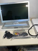 Coby portable DVD player with screen flipped down, showing front panel and accessories in front including power adapter, AV cables, and remote control wrapped in plastic.