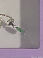 Close-up of pendant showing three green emerald stones set in silver in a vertical arrangement on a silver chain.