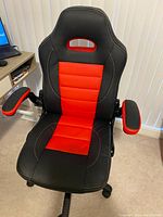 Black and red gaming chair with ergonomic design, padded armrests, high back with headrest cutout and wheels underneath.