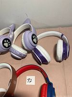 Two purple and white wireless headphones with paw print design, placed on a bed or fabric surface.