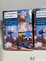 Box front showing Max Projects snowflake motion light projector with cool white and blue lights projecting snowflakes up to 65 feet indoors or outdoors.